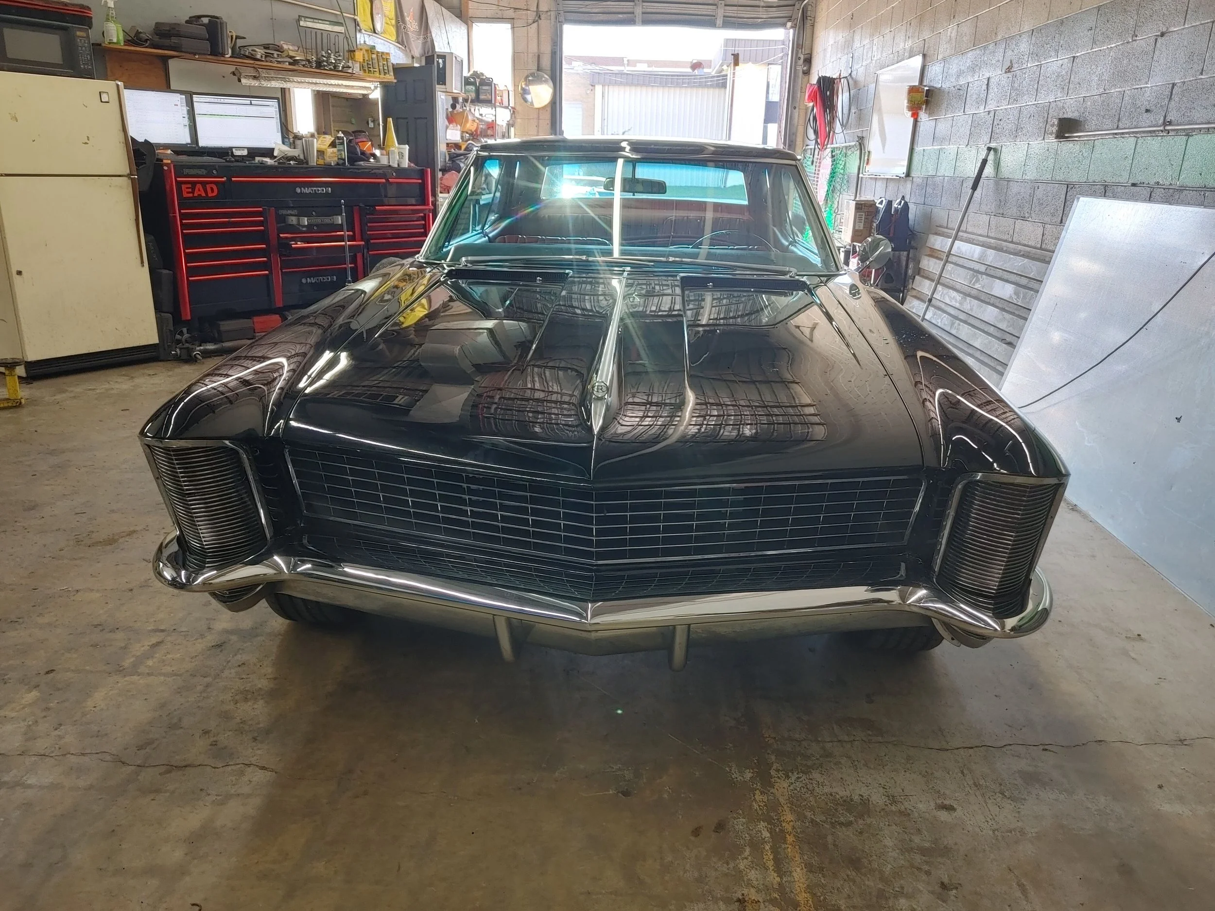 Black vintage car inside a garage with tools and shelves in the background.