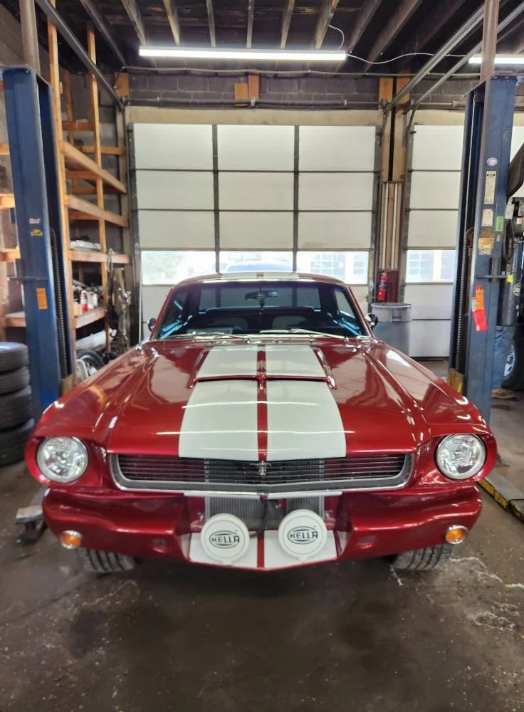 Red vintage muscle car with white racing stripe in garage.
