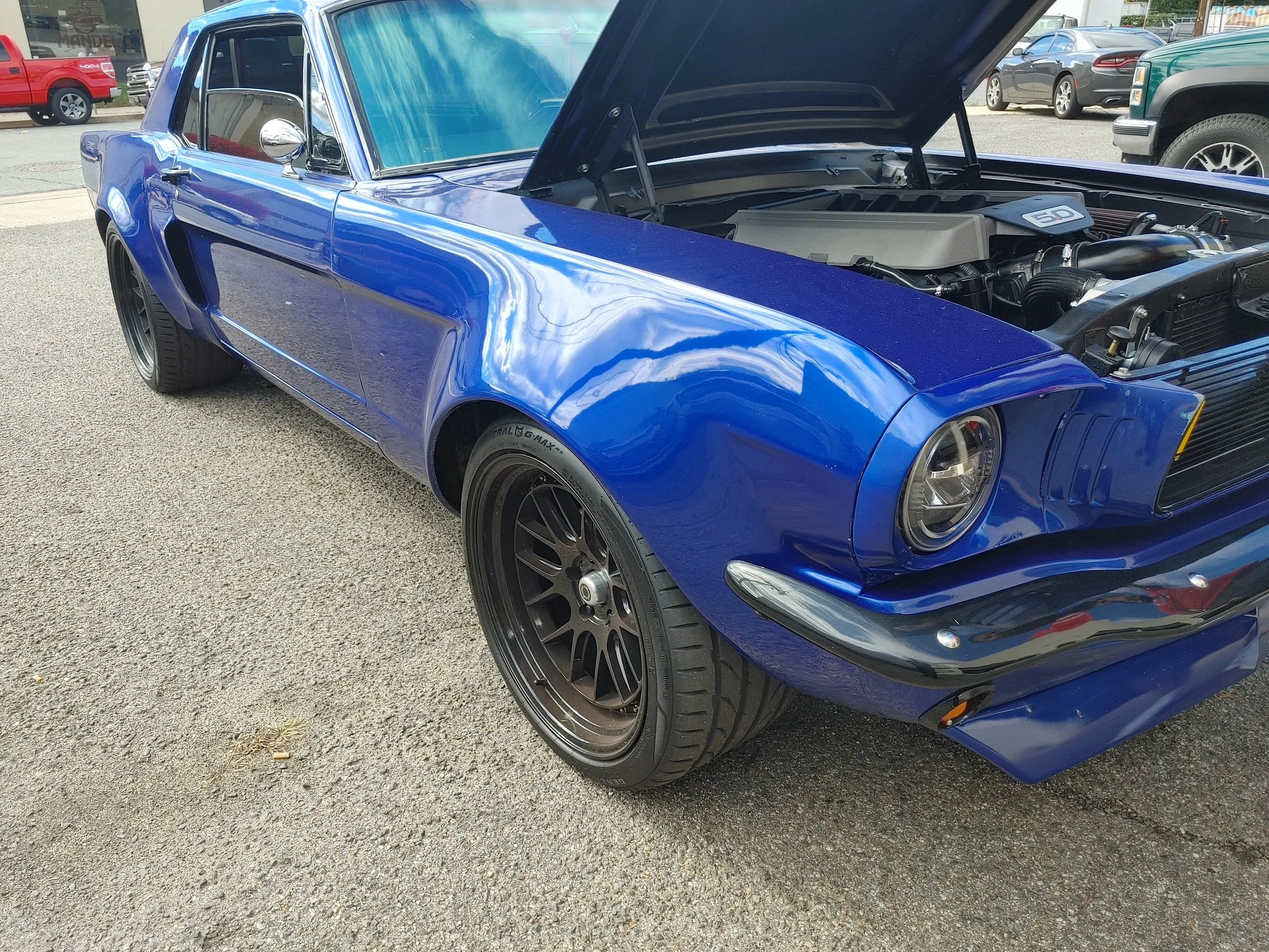 A vintage blue muscle car with open hood parked on the street, showcasing its engine.