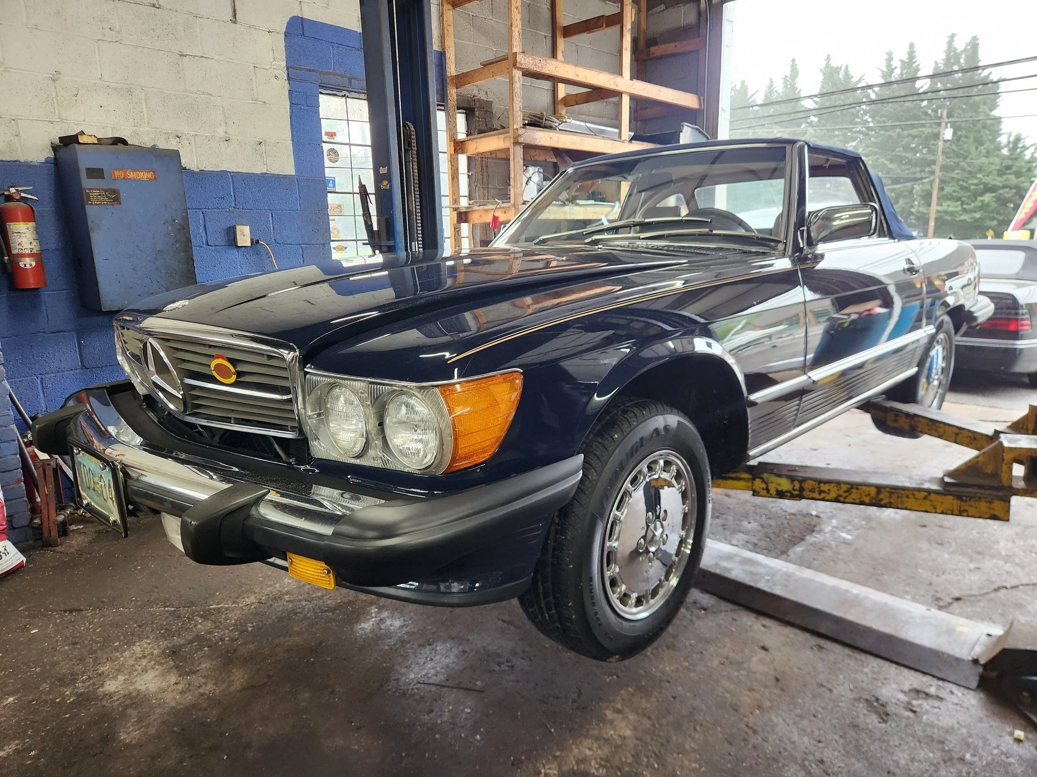A classic Mercedes-Benz convertible parked inside a garage, with a dark exterior and vintage wheel design.