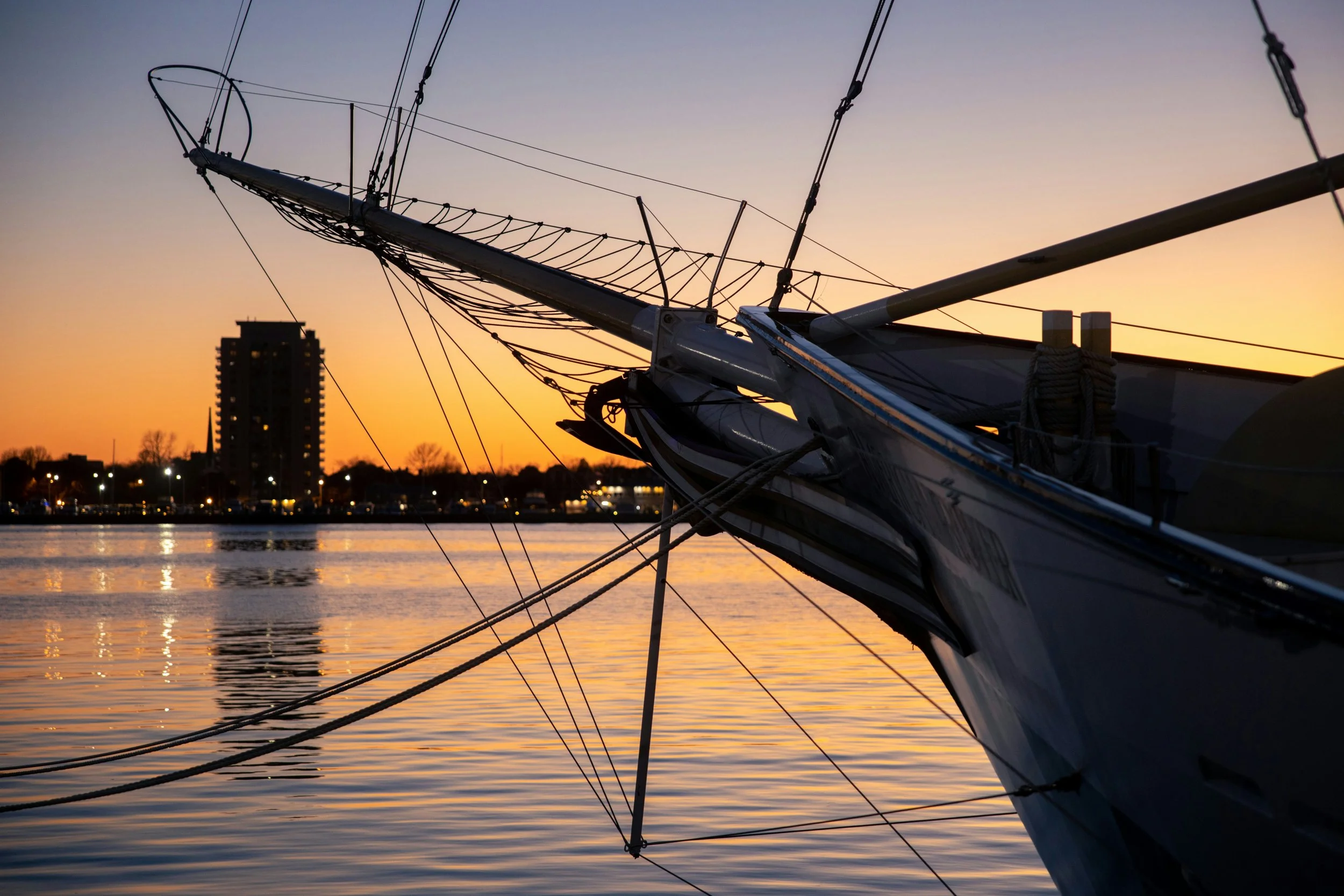 Sailboat moored in calm water during sunset, with city skyline and tall building in the background.