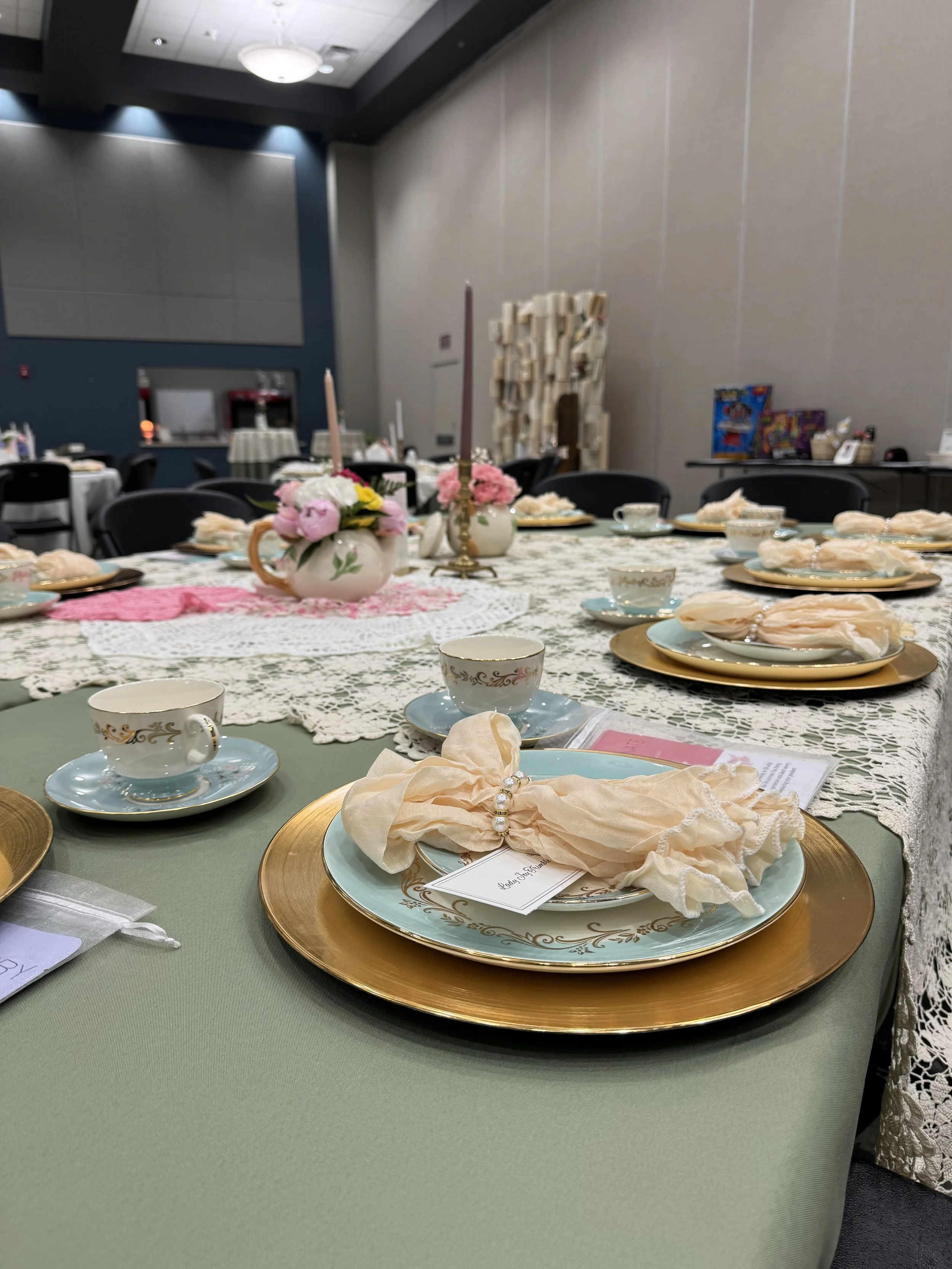 Decorated table set for a gathering with fine china, pink and cream napkins, flowers, and candles in a banquet hall.
