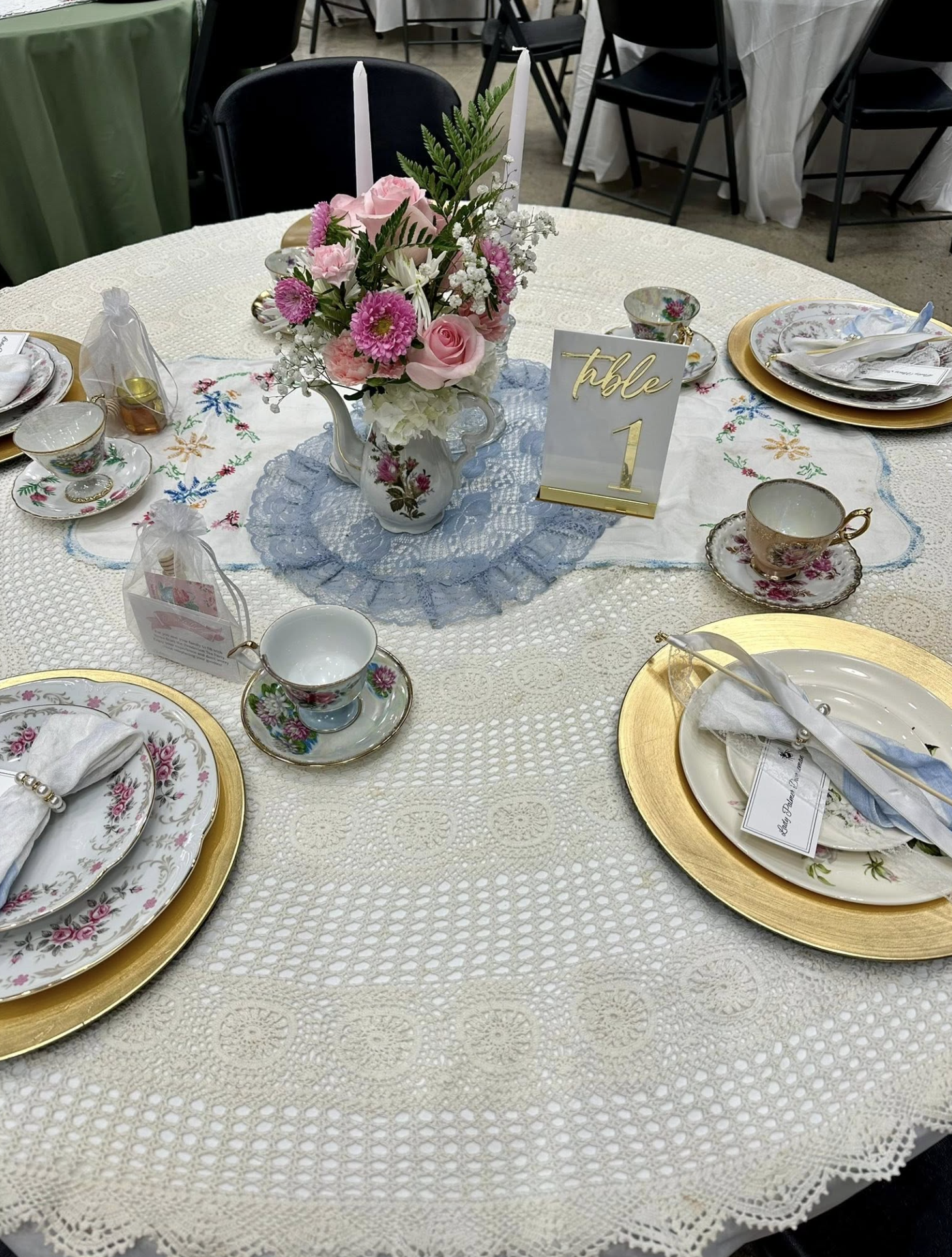 Elegant table setting with floral china, gold chargers, a central floral arrangement, and a table number sign, for a formal event.