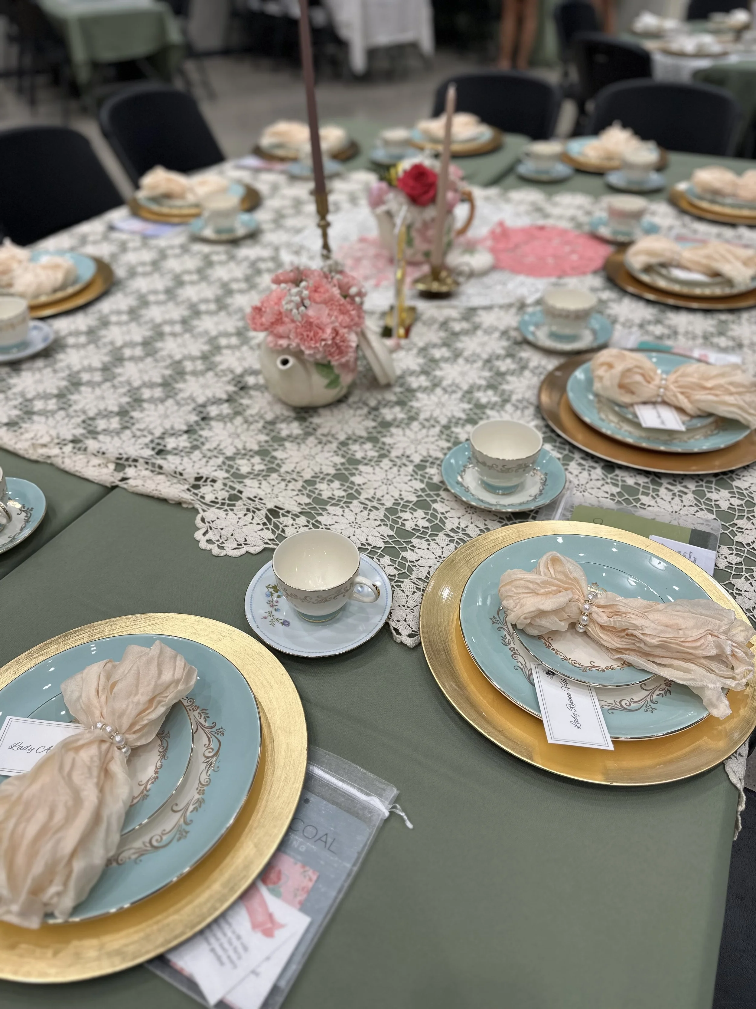 Table set for tea party with pastel-colored plates, cups, and napkins, decorated with pink flowers and candles.