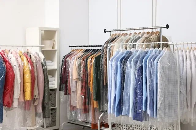 Clothing store with racks of colorful shirts and jackets covered in plastic, and white shelves with folded clothes in the background.