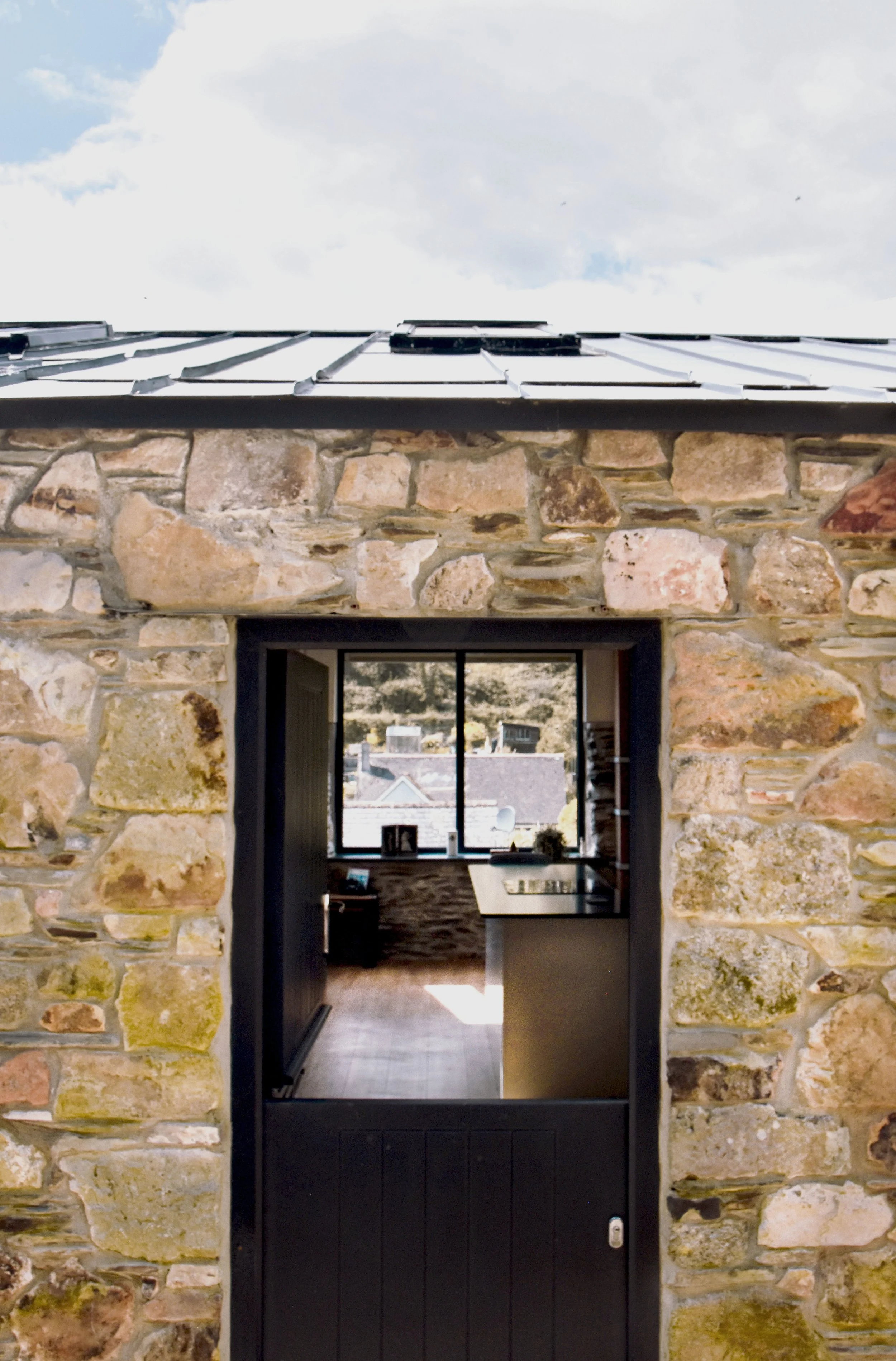 View through an open black door into a room with a window, showing a rural landscape with buildings and hills outside.