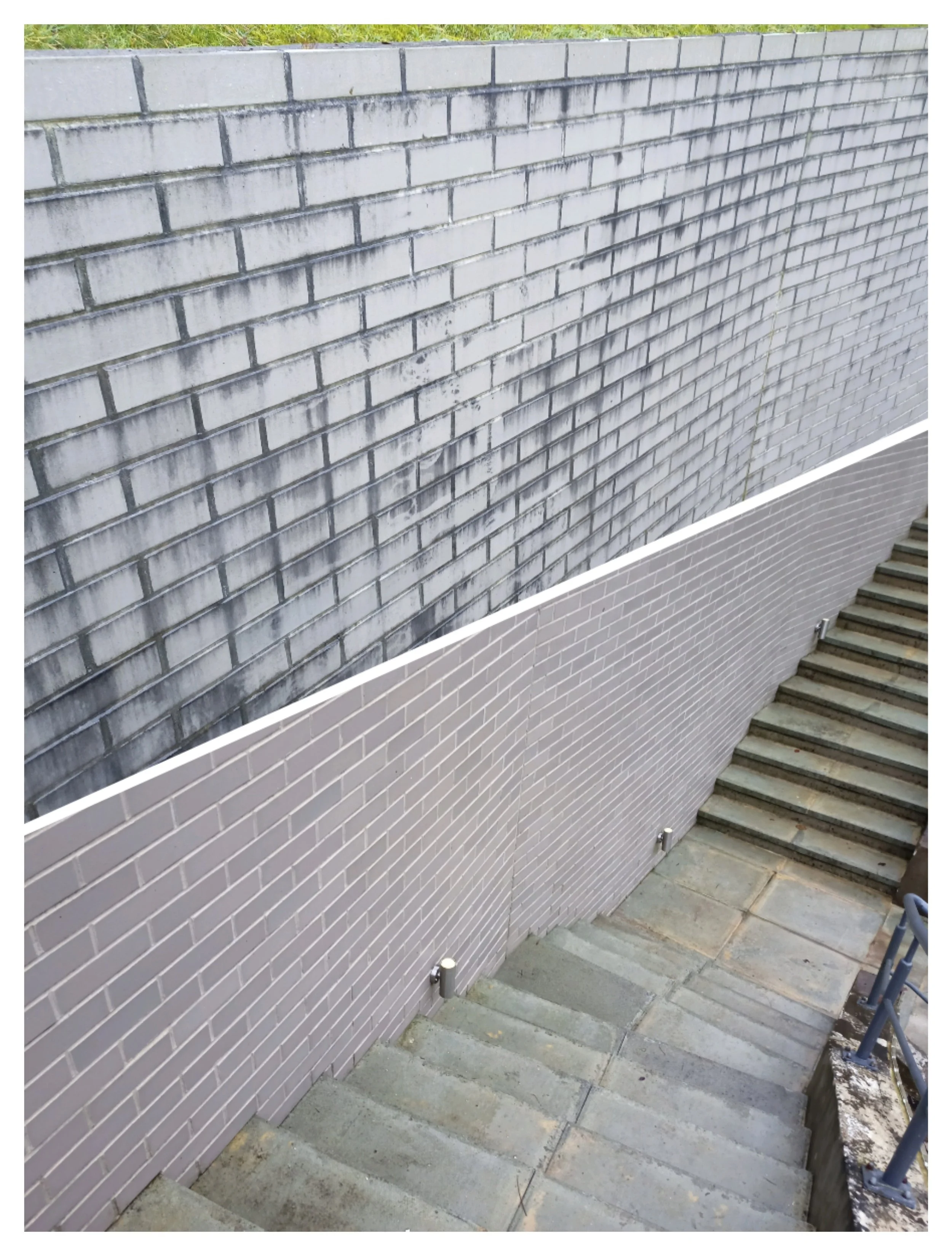 A concrete staircase with steps leading downward along a brick wall with two small outdoor lights at the base of the wall.