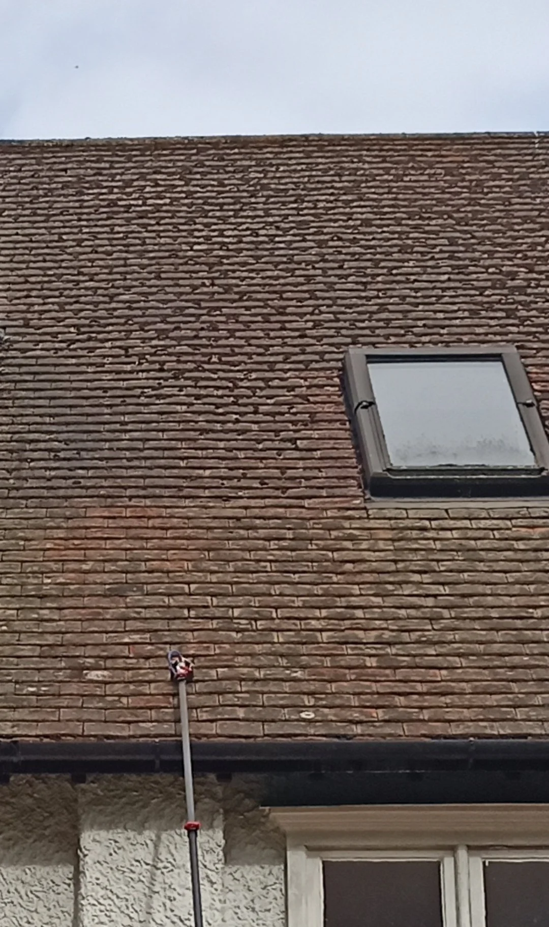 A brick house roof with a skylight window and chimney pipe.