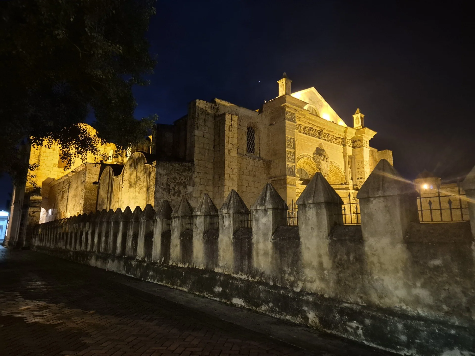 A historic old building illuminated at night with a stone fence in the foreground and a dark sky above.