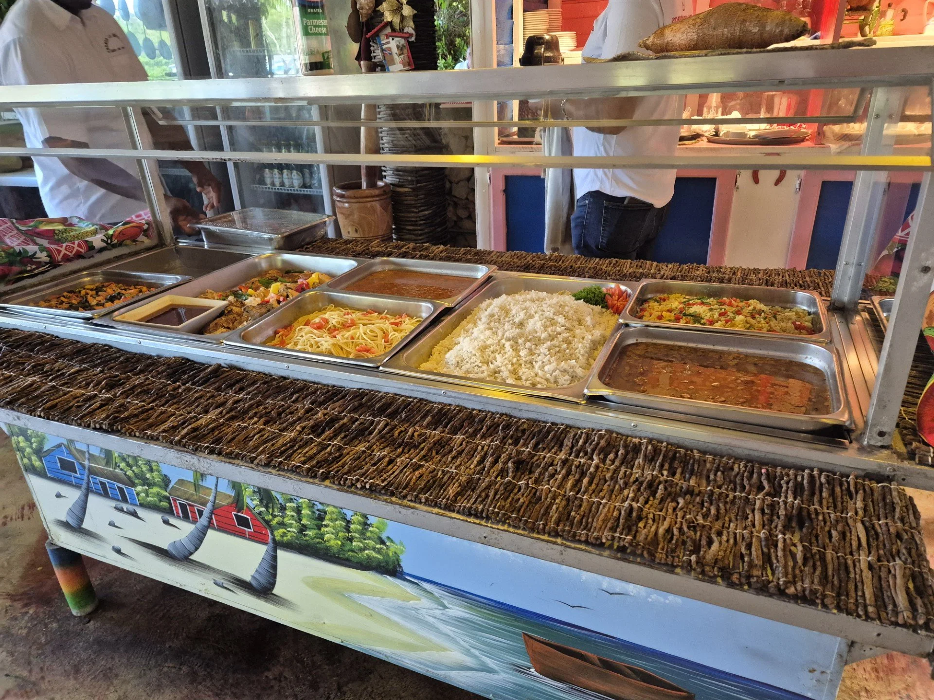 A food stand with various dishes including rice, pasta, and stews, behind a glass shield in a restaurant or street vendor setting.