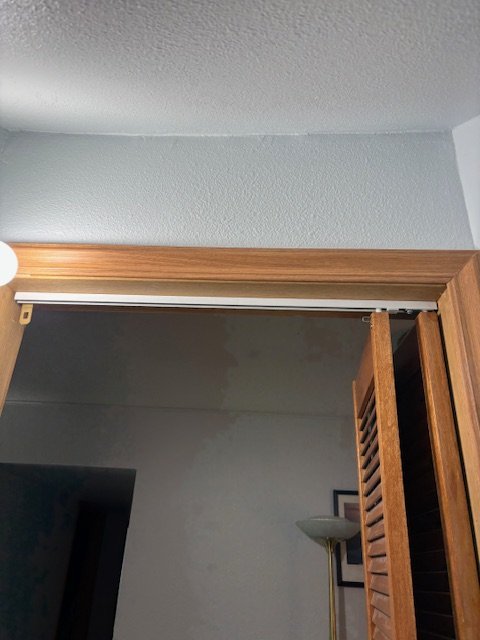 Part of an interior room showing a wooden door, a wooden door frame, a wall with a picture frame, and a standing lamp.
