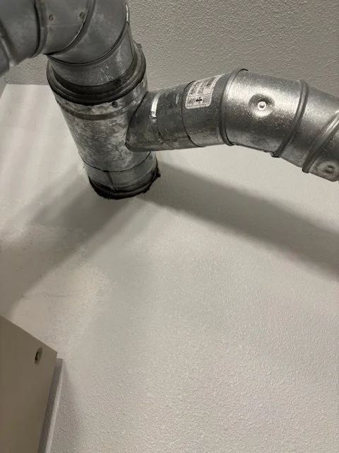Close-up of industrial metal pipes attached to ceiling with white textured wall background.