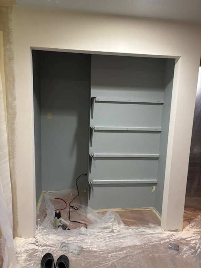 Empty recessed shelf with three built-in shelves in a wall, with some tools and plastic sheeting on the floor.