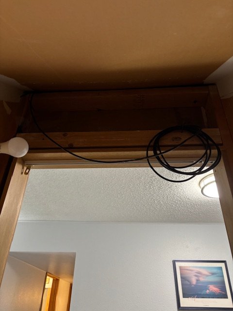 A partially installed or removed hanging light fixture with exposed wires above a doorway, with a painting visible on the wall in the background.