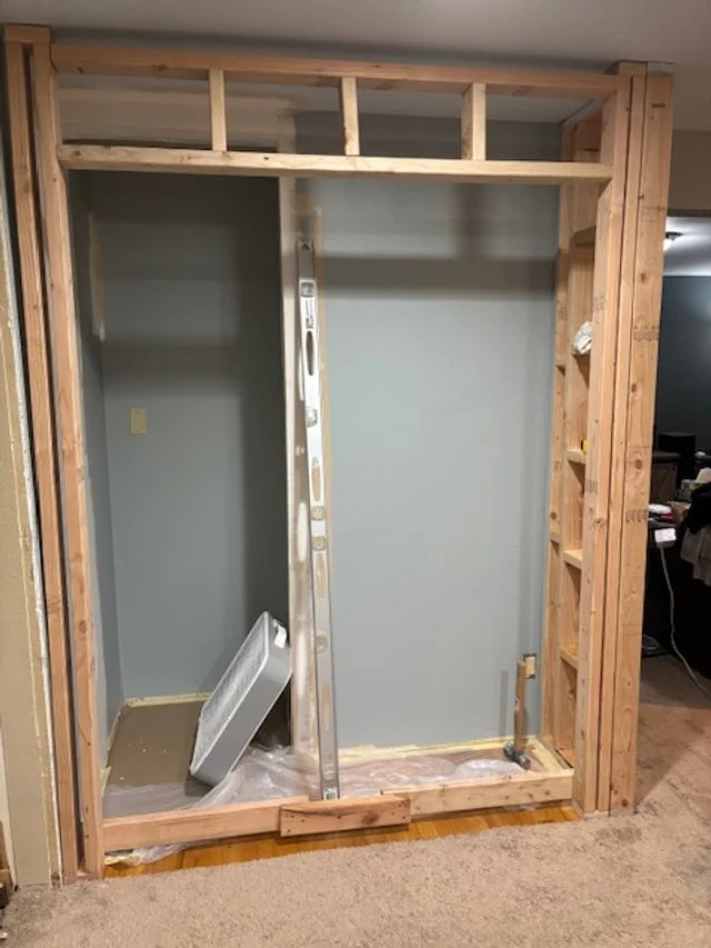 Unfinished wall frame with exposed wooden studs and a drywall panel, room construction in progress.