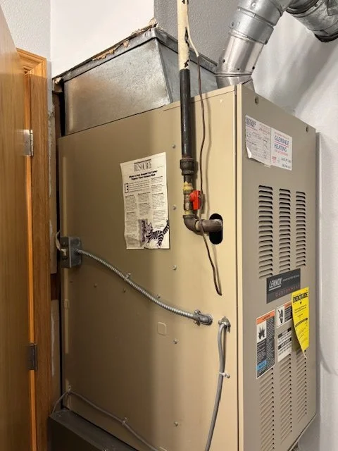A beige furnace unit installed in a closet next to a wooden door, with a metal vent pipe connected at the top.