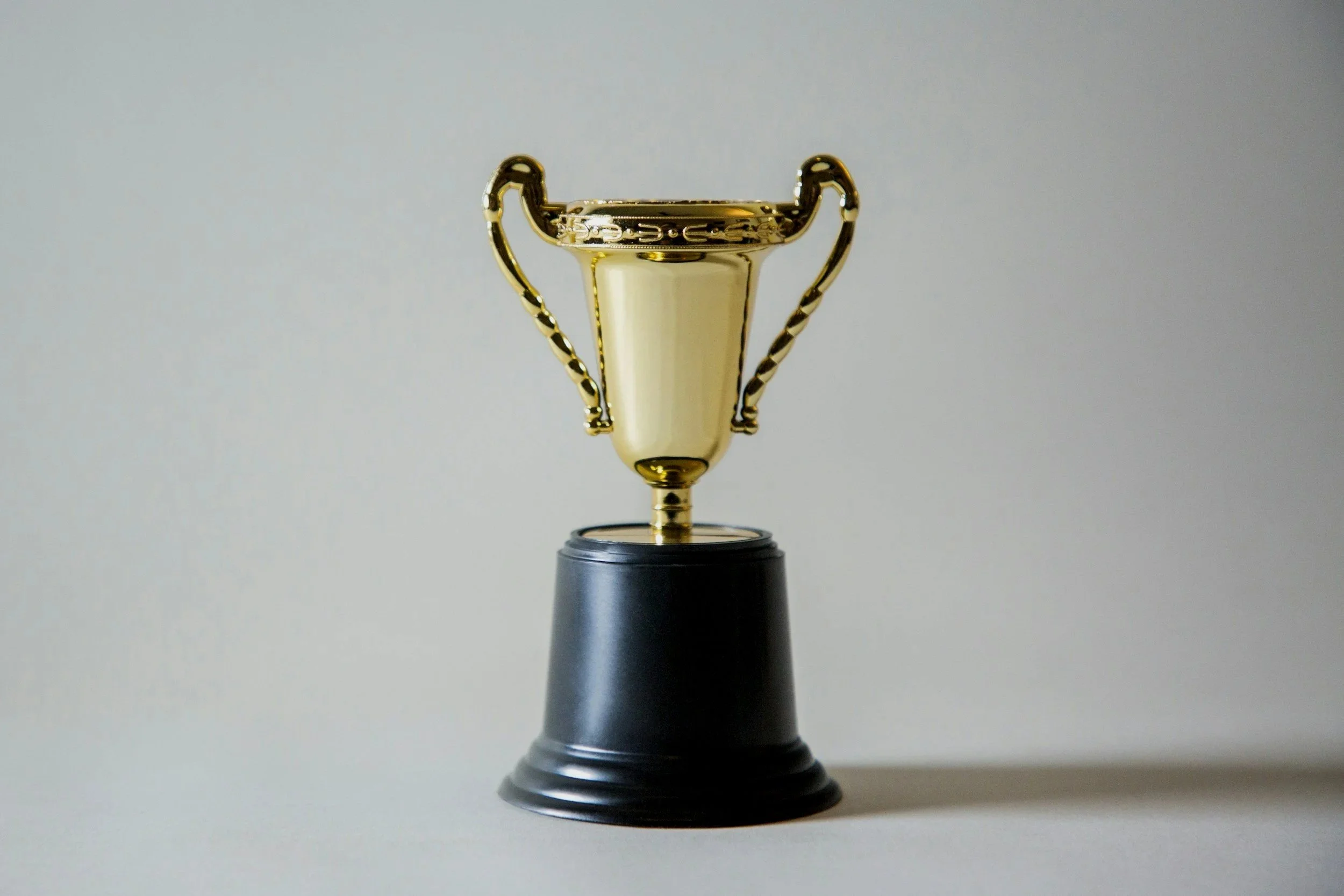 Golden trophy cup on a black base against a plain light background.