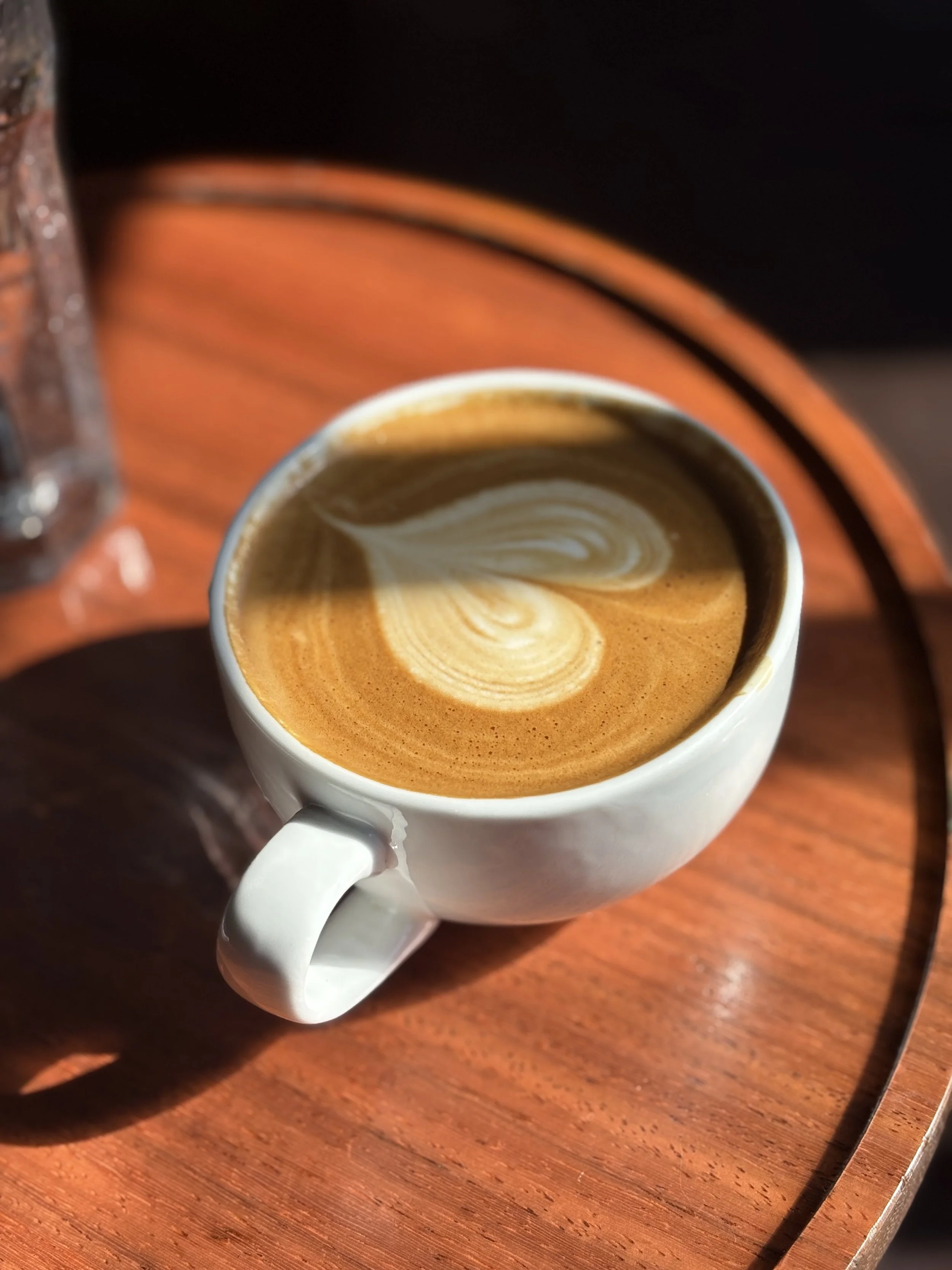 Flat white coffee on a wooden table in warm sunlight — slow travel and intentional living with travel astrology, astrocartography, astromaps and travel experiences guided by astrology