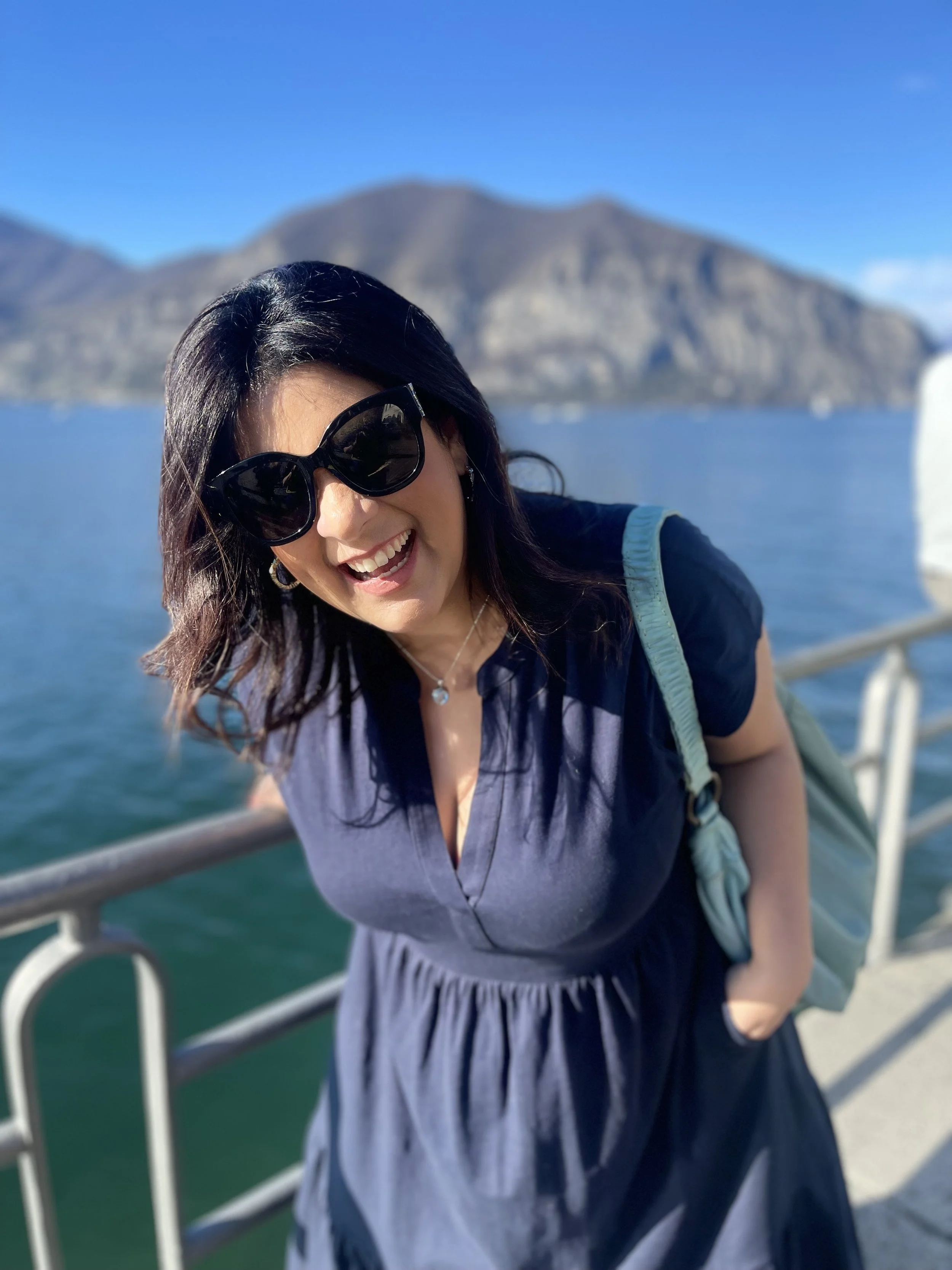 Natalia, founder of Cosmic Travel Studio, smiling by the water with mountain views — astrocartography reader and astrology travel curator