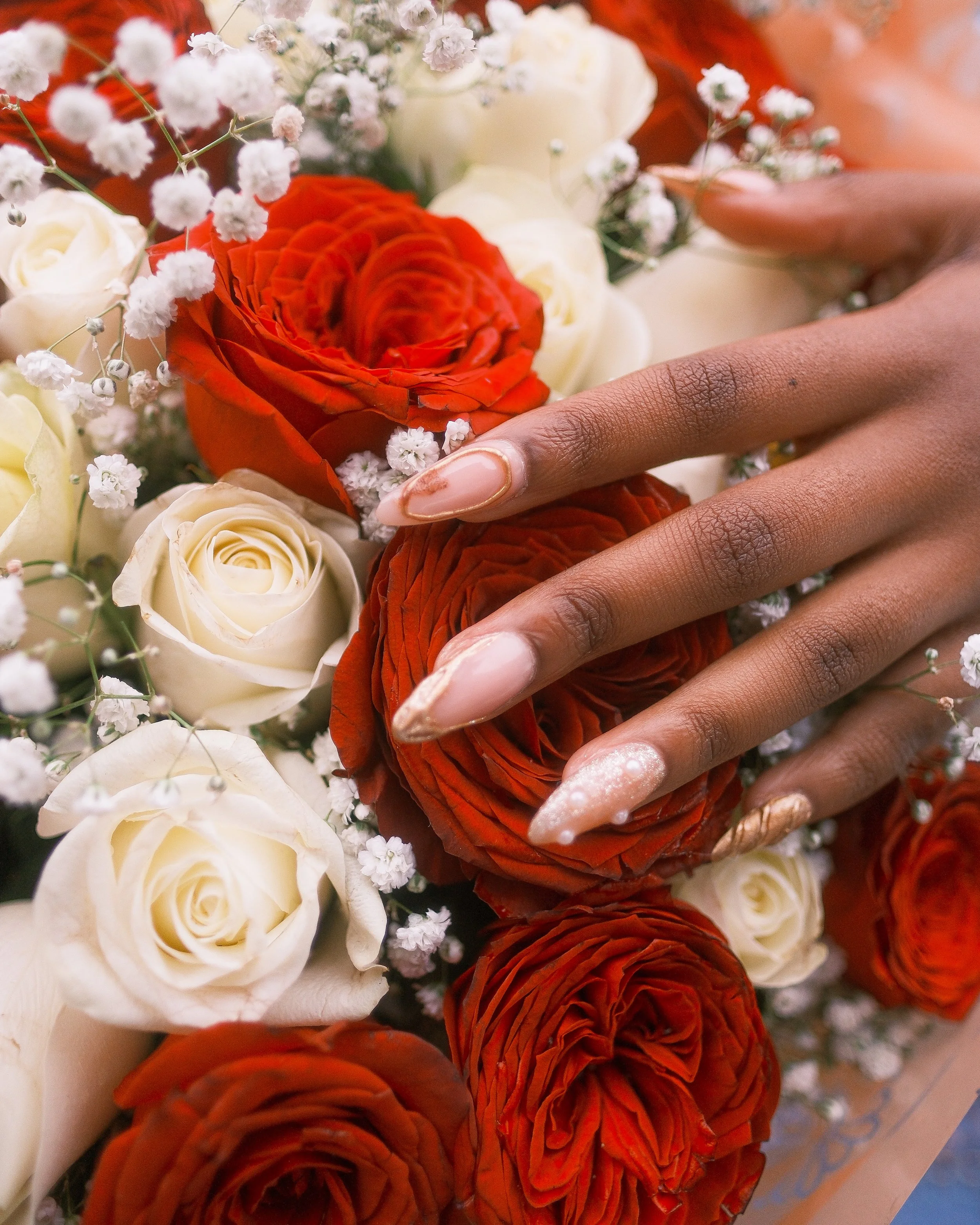 Close-up of a hand with manicured nails resting on red and white roses, surrounded by small white baby's breath flowers.