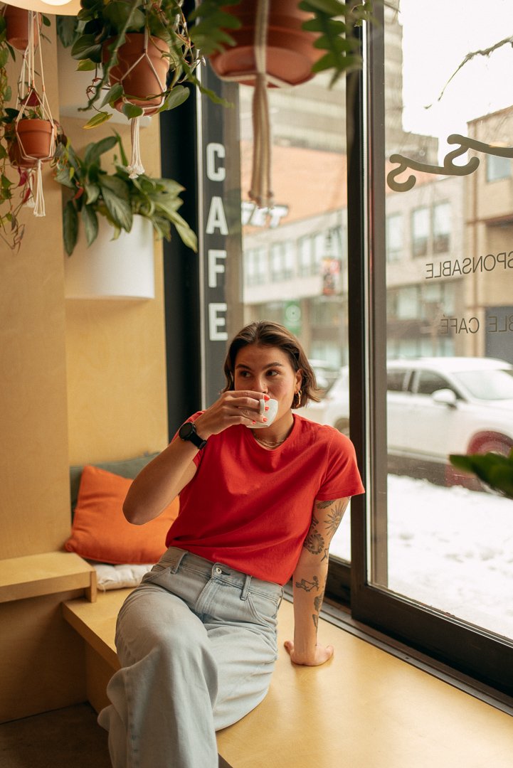 A middle-aged man with slicked-back gray hair sitting on a beige cushioned bench against a plain wall, wearing a blue short-sleeve sweater and beige pants, looking thoughtfully to the side.