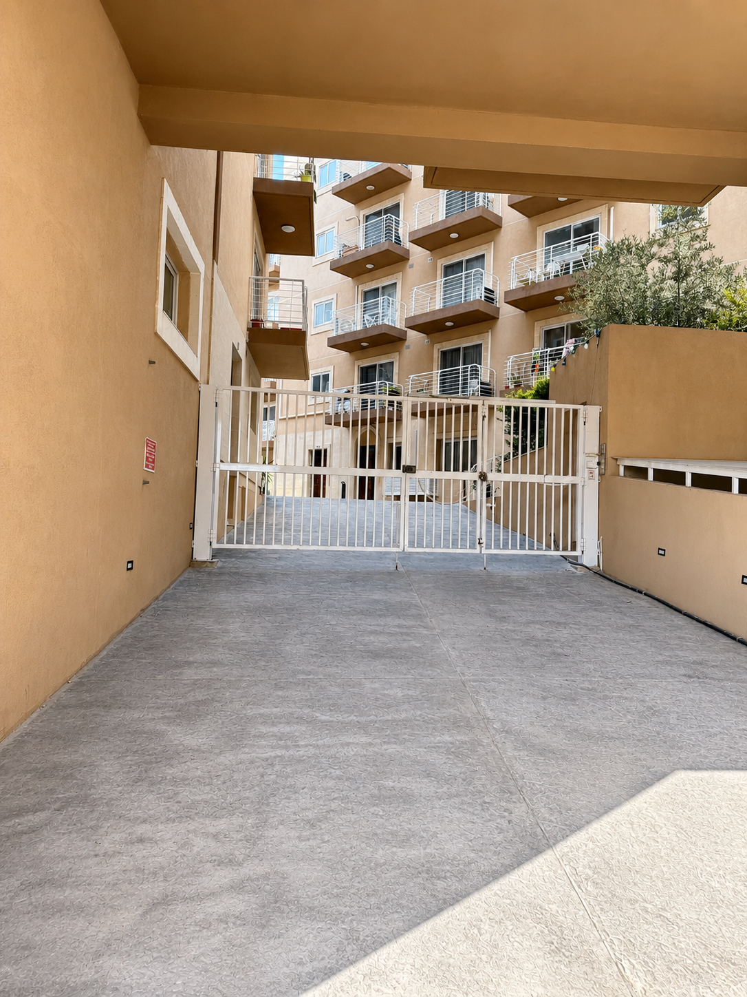 View of an apartment complex courtyard with a white gated entrance, multiple balconies with railings, and beige walls.