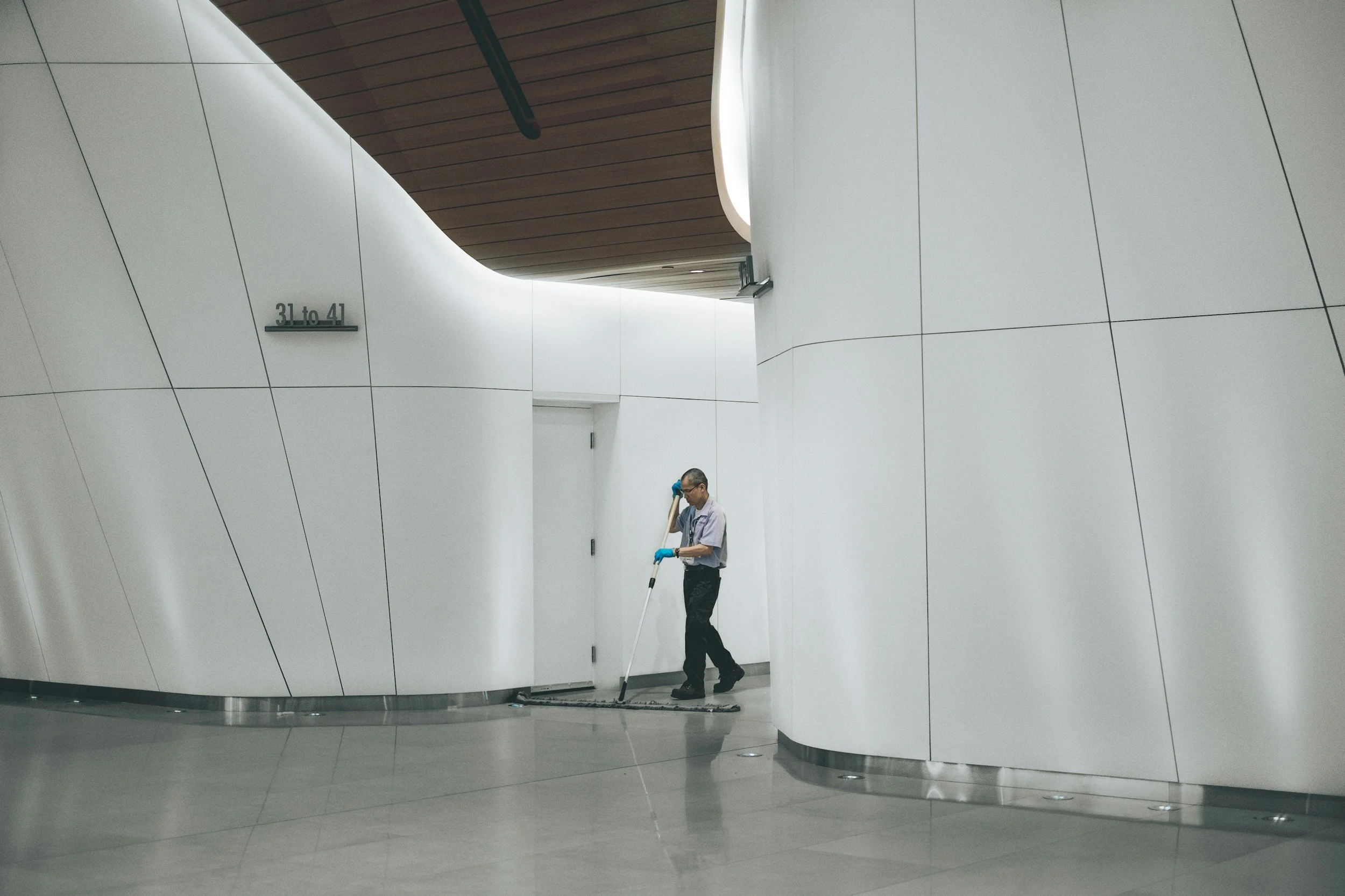 Ein Mann reinigt den Boden in einem modernen, weißen Architektur-Gang mit einer Kehrmaschine.