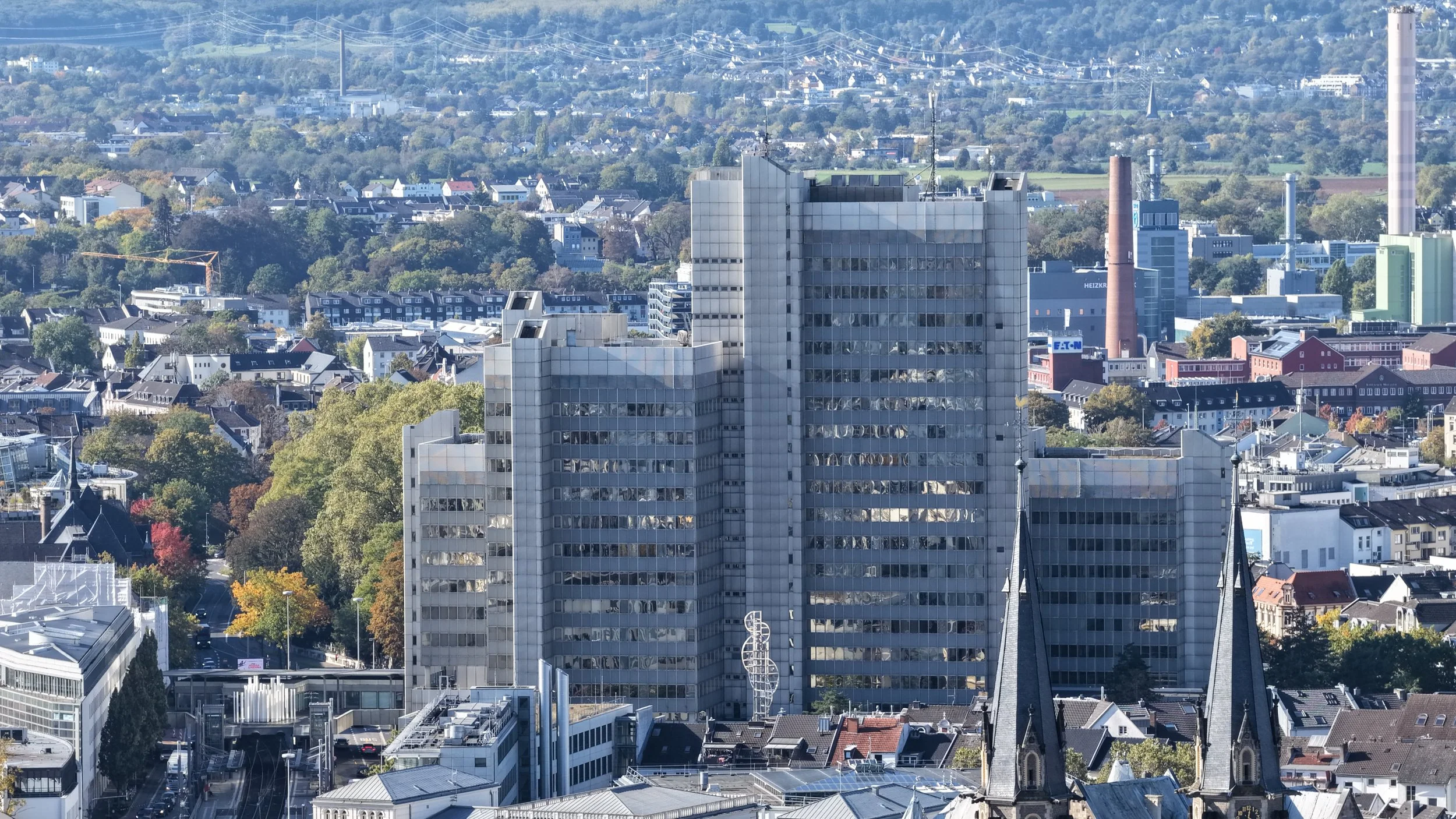 Stadt mit hohen Gebäuden und umgebender Natur, im Hintergrund ein Hügel mit vielen Häusern und Bäumen.