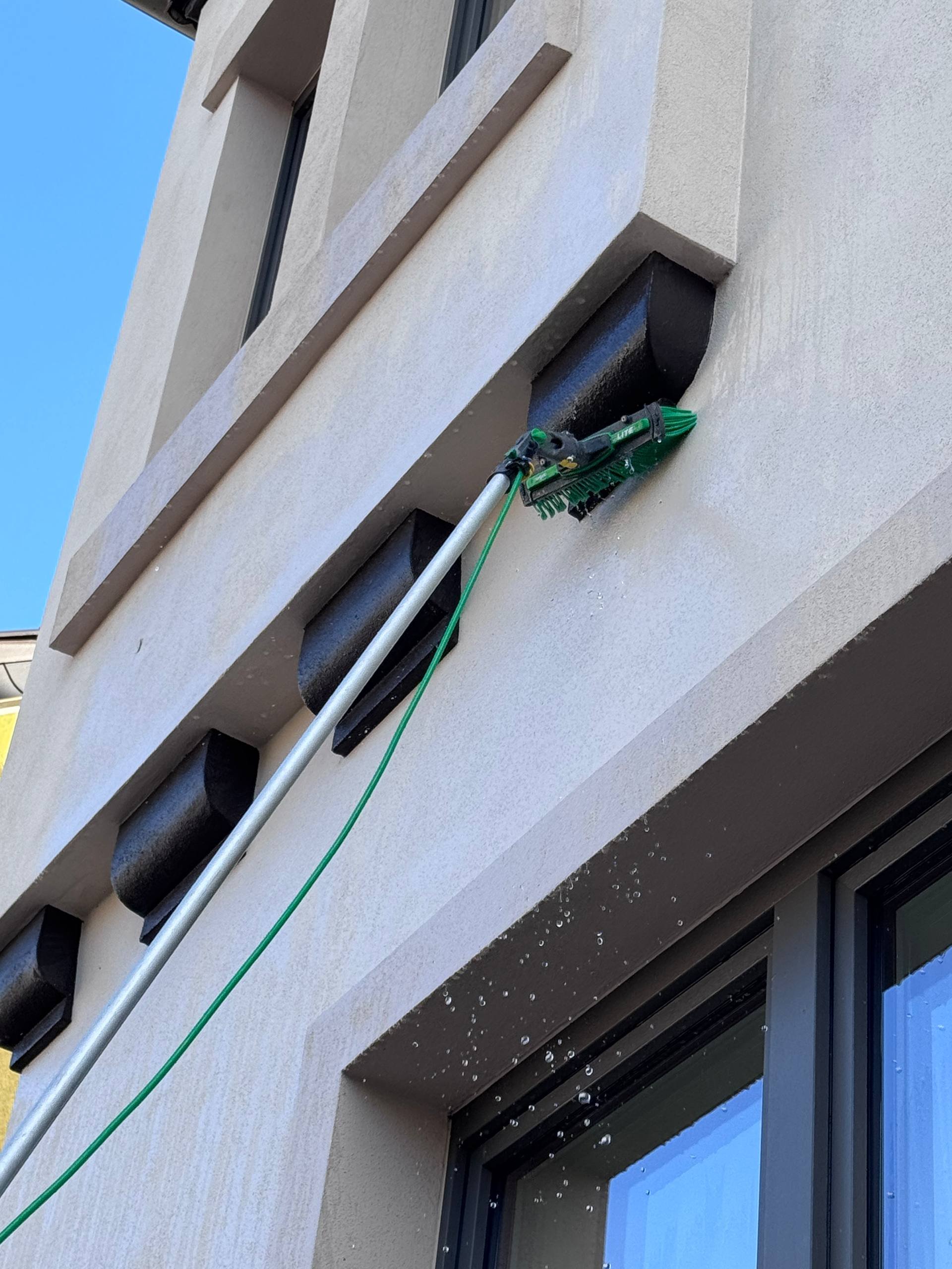 Fenster und Lüftungsschlitze an der Außenfassade eines modernen Gebäudes, mit Wasser, das von einem Reinigungsgerät herunterläuft.