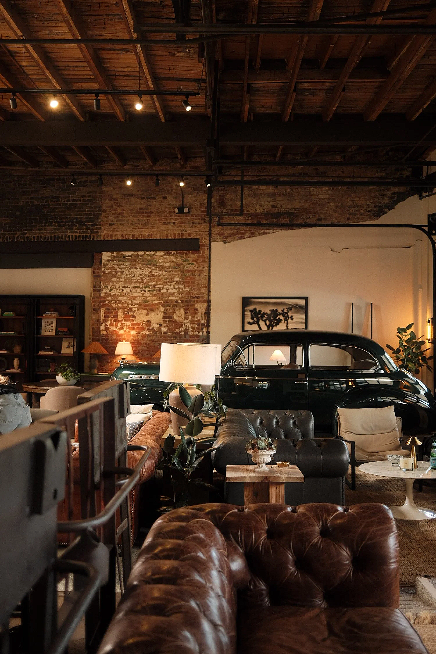 Interior of a stylish living space with vintage decor, a black classic car, leather sofas, a bookshelf, and warm lighting.