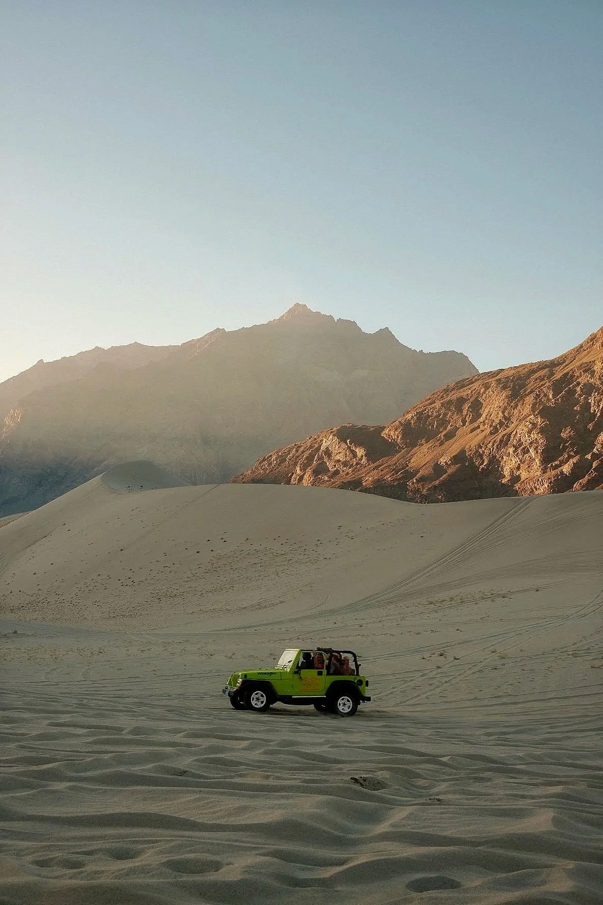 A green toy Jeep in a desert with sand dunes and mountains in the background.
