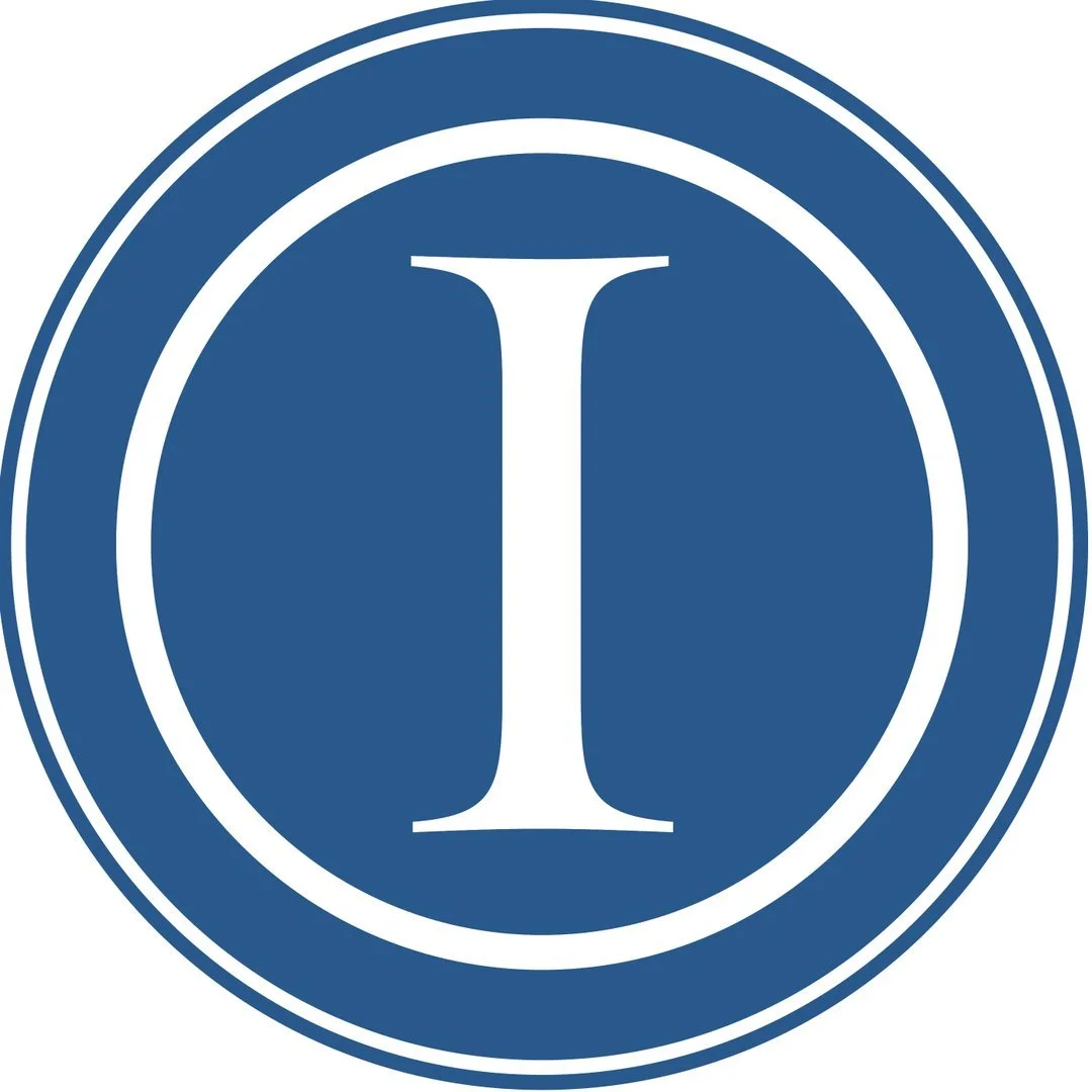 A circular logo with a dark blue background and a white border. Inside, a large white letter 'I' is centered.