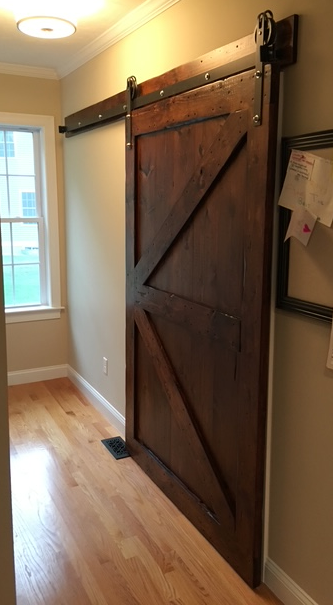 Custom wooden sliding barn door on a metal track in a room with hardwood floors and a window.
