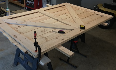 Custom made wooden door panel with tools, measuring tape and clamps on workbench in workshop.