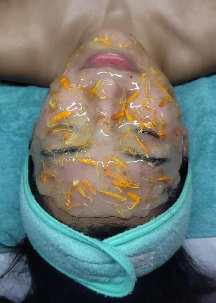 A person lying down with a facial treatment mask infused with yellow flower petals and a turquoise headband.