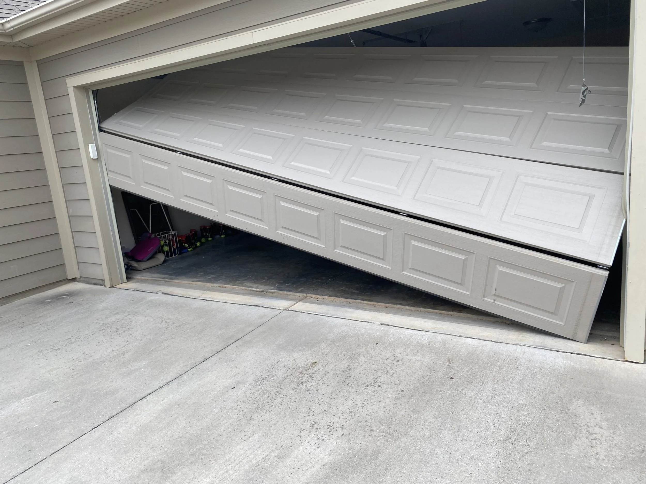 A garage door partially open, tilted downward on one side, revealing stored items inside.