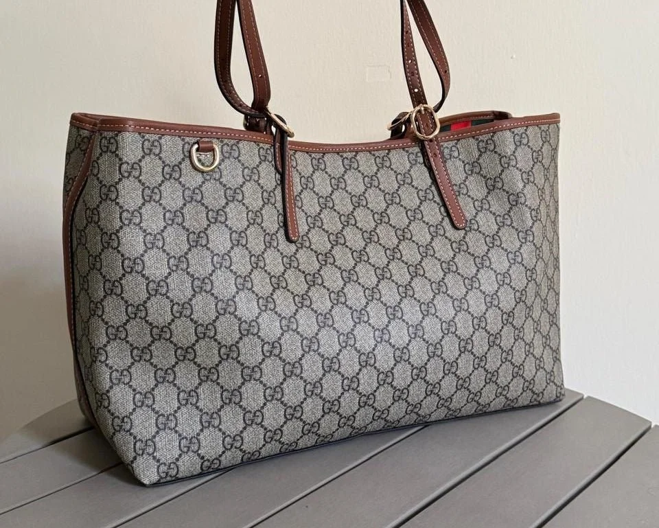 A large designer tote bag with the Gucci monogram pattern resting on a gray table.