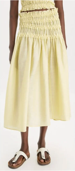 A woman wearing a yellow, ruched, strapless skirt and white sandals with dark soles.