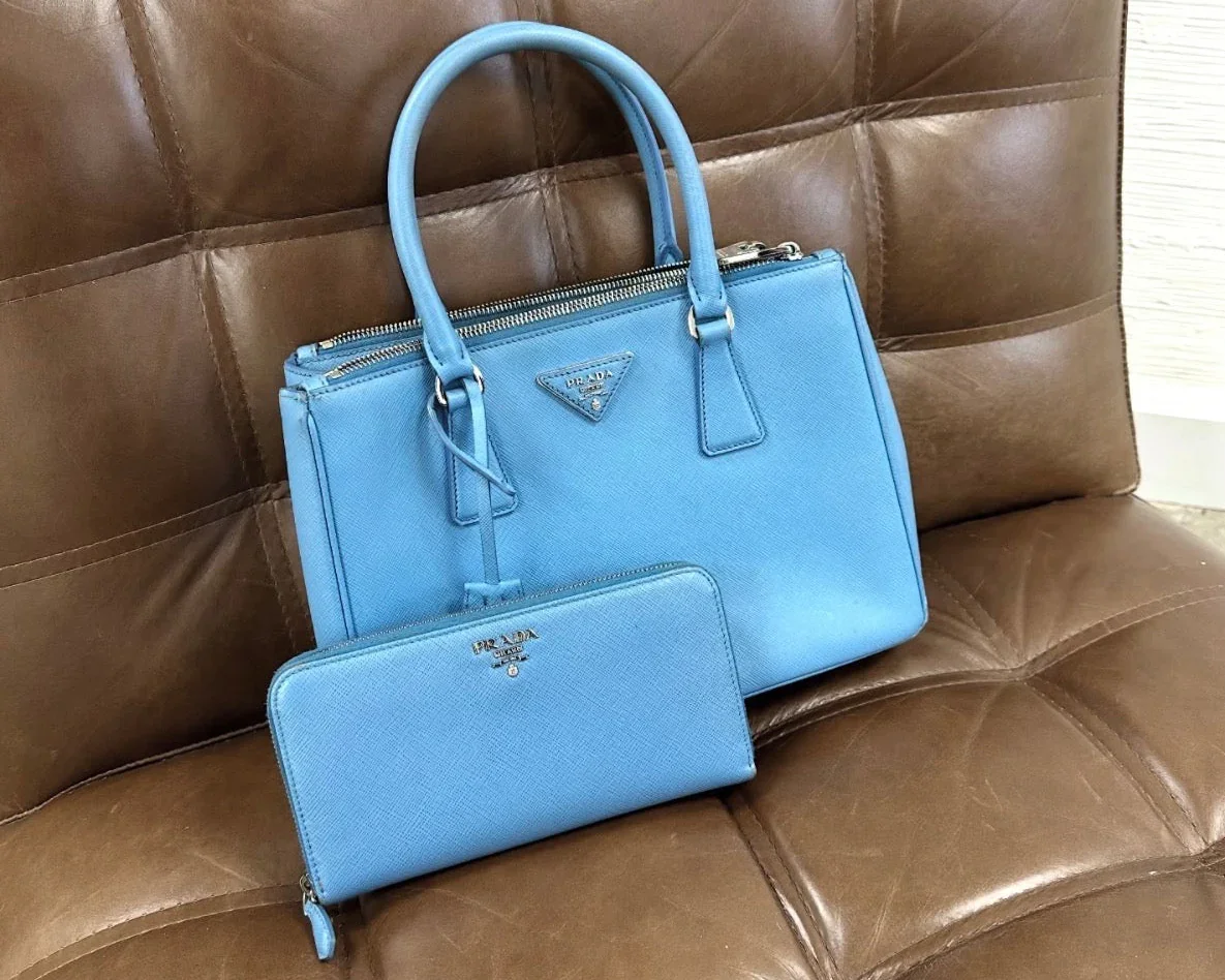 A blue Prada handbag and matching wallet placed on a brown leather sofa.