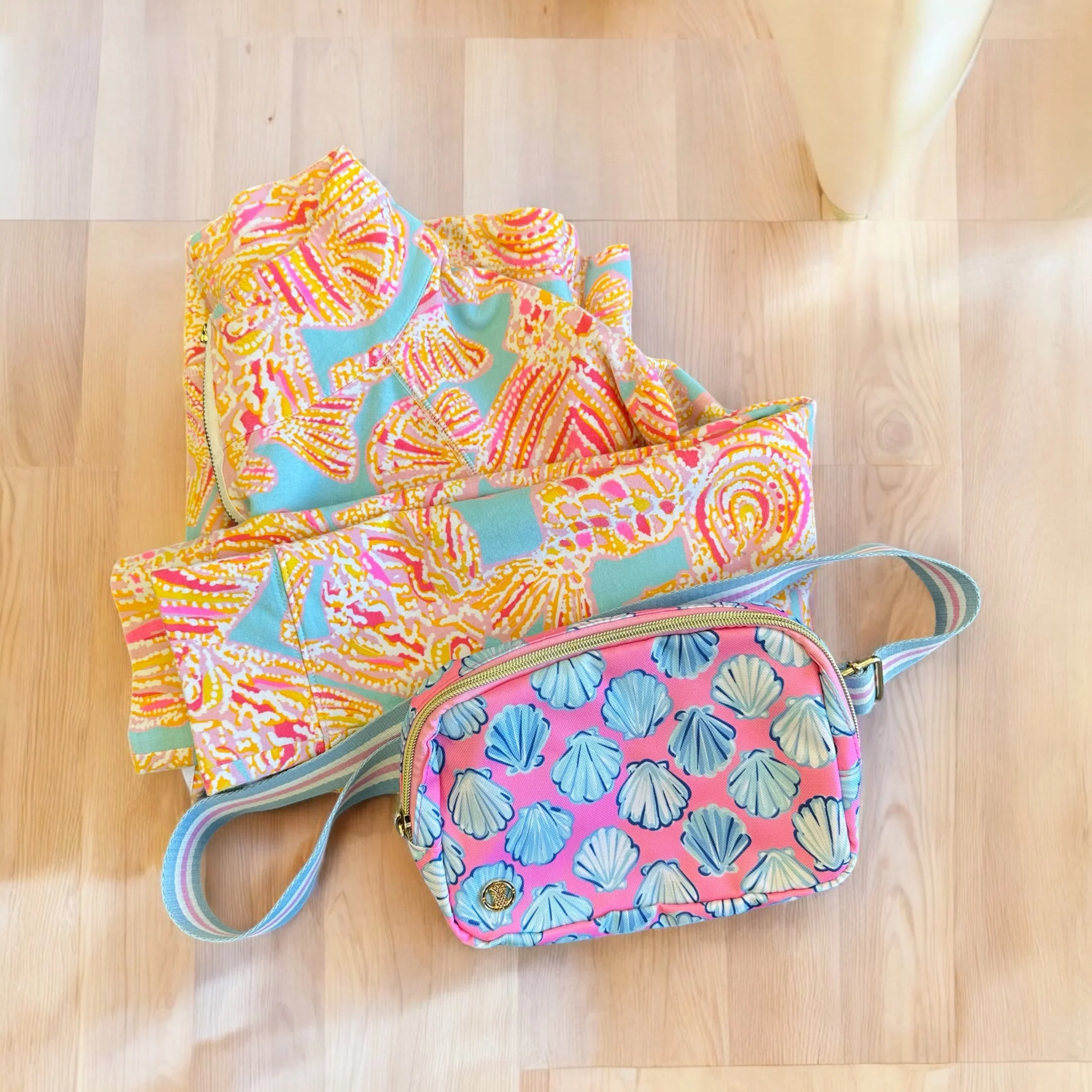 Bag with scallop shell pattern, colorful fabric with pastel blue, pink, and white shells on a pink background, placed on a light wooden floor.