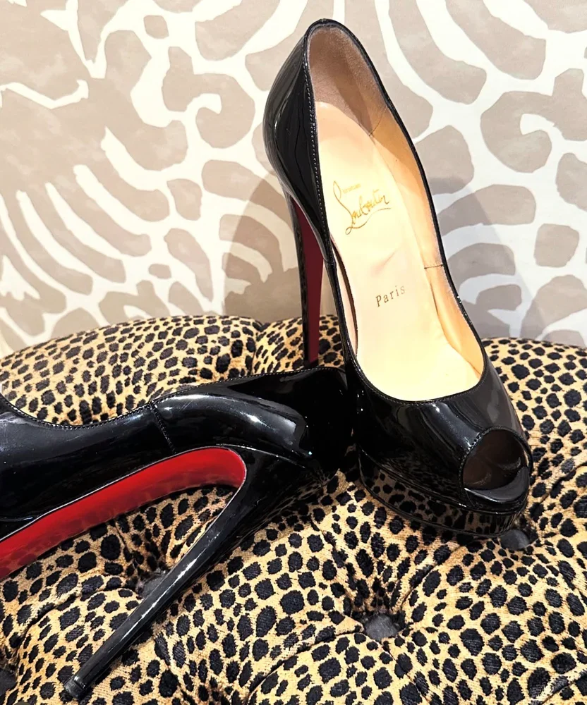 A pair of black Christian Louboutin high heels with red soles, placed on a leopard print fabric surface.