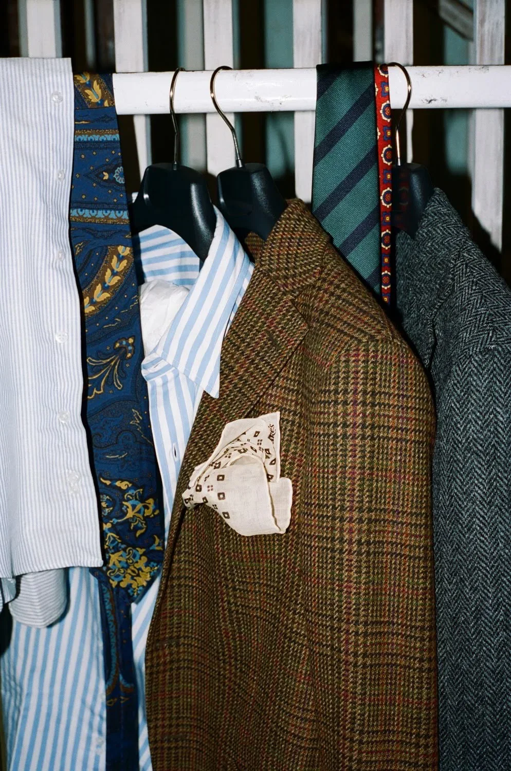 A collection of men's clothing, including shirts, jackets, and ties, hanging on a white clothing rack with black hangers.