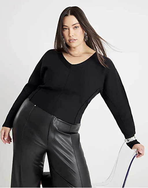 Woman in black sweater and black leather pants posing against a plain background.