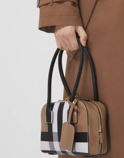 A person dressed in brown holding a stylish brown, beige, black, and white striped handbag with a small matching pouch