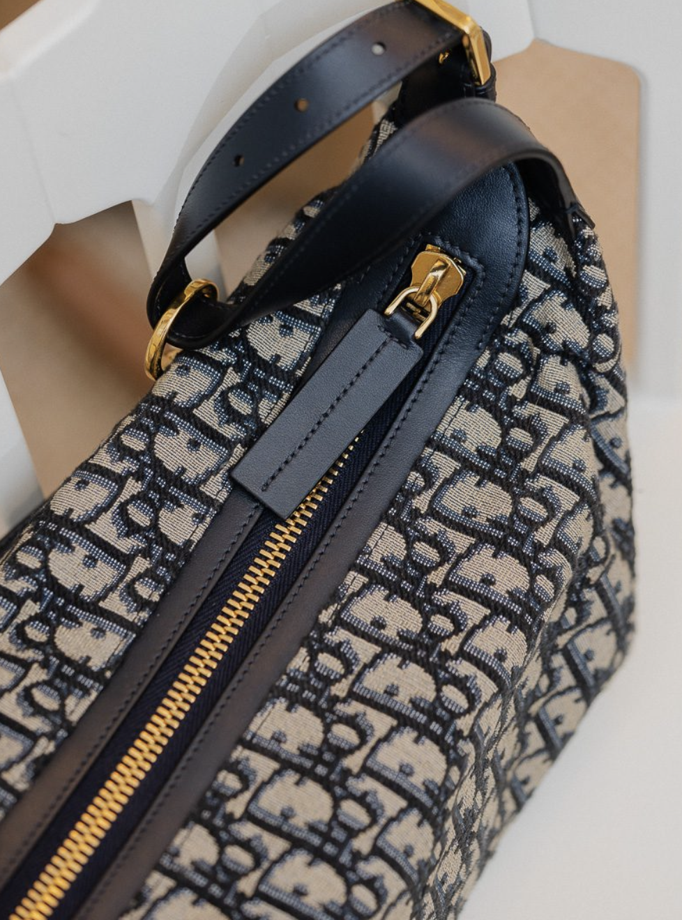 Close-up of a designer handbag with a patterned fabric, gold zipper, and black leather accents and handle.