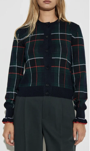 Woman wearing a dark plaid cardigan with navy, red, and green stripes, buttoned up, with dark pants.