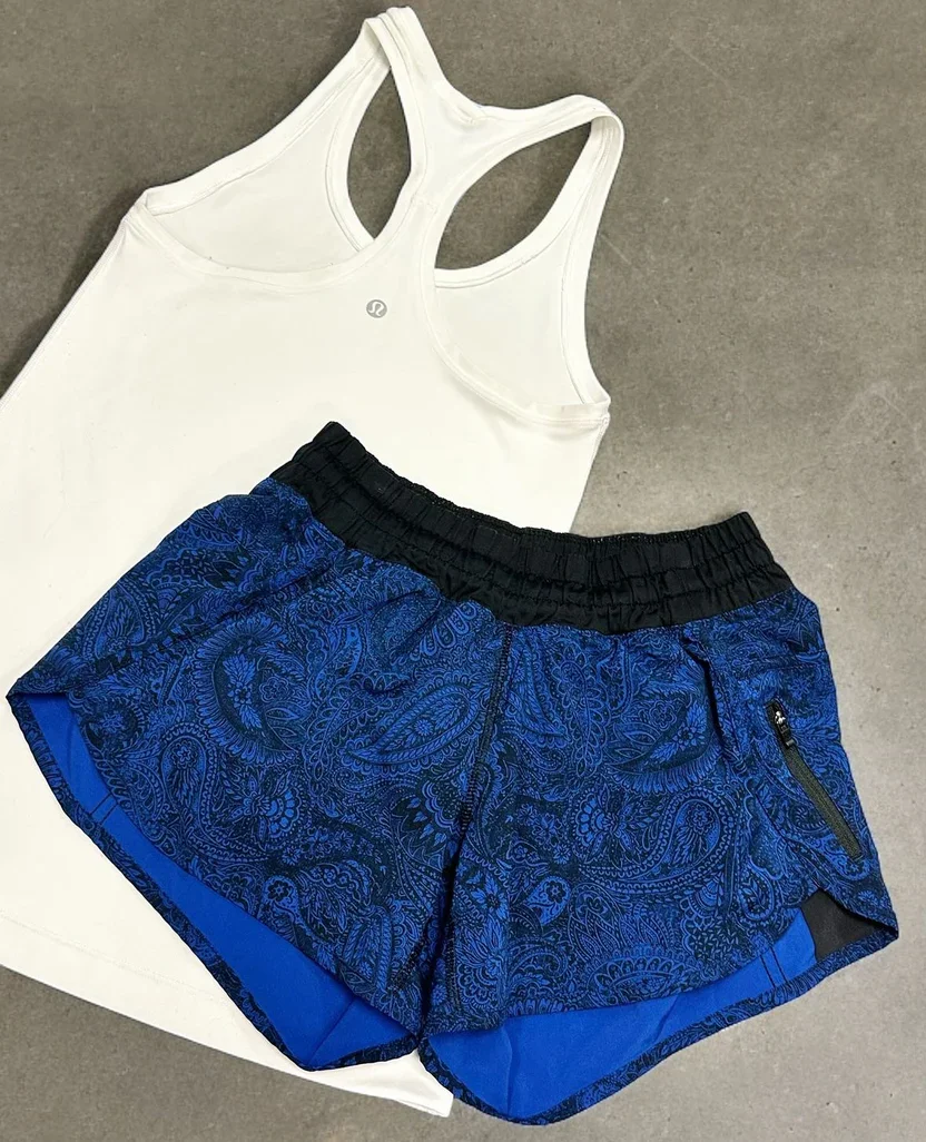 A white athletic tank top and blue patterned running shorts with a zippered pocket, laid out on a gray surface.