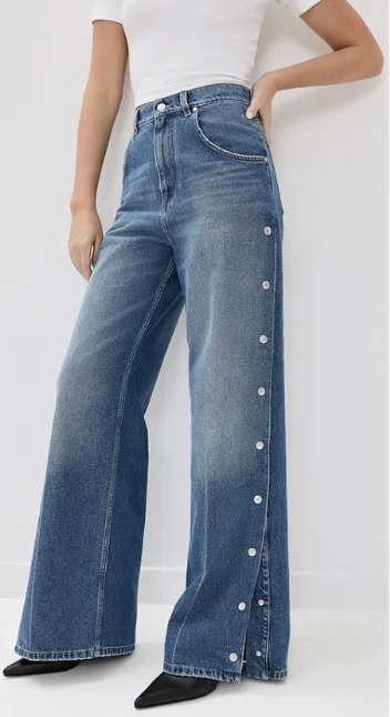 A person wearing wide-leg blue jeans with buttons along the side, paired with a white top and black shoes.