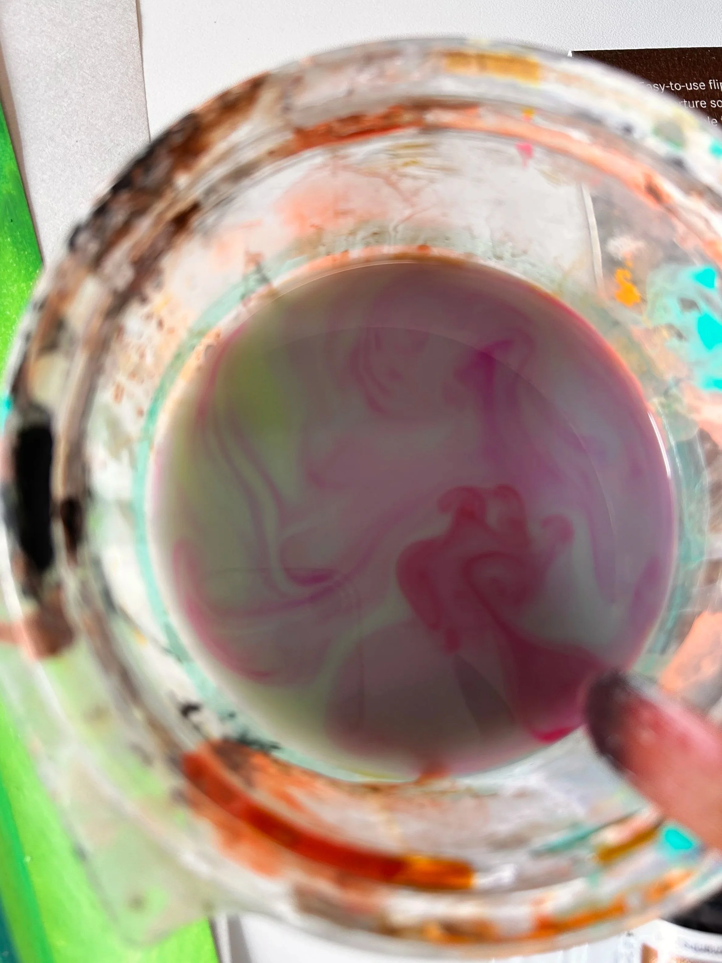 Close-up view of a stained glass glass with colorful swirls and a small fingertip at the edge.