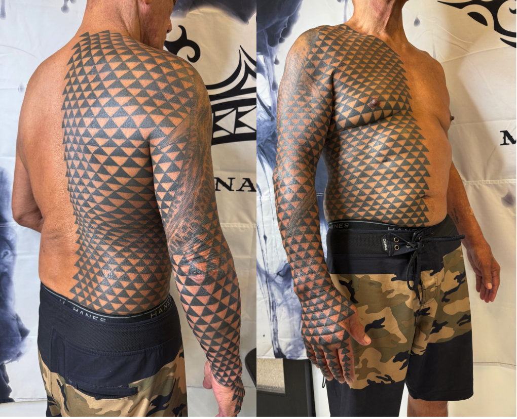 A man with a large geometric Polynesian inspired tattoo covering his shoulder, arm, and side, standing shirtless in front of a white background. He is wearing camouflage shorts and black waistband, with a similar tattoo design on his right hand.